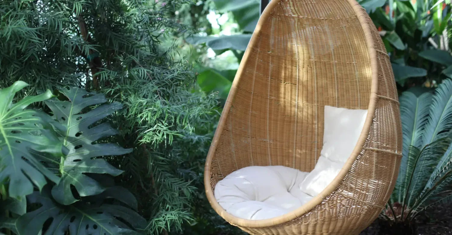 Egg-shaped wicker hanging chair with white cushion for stylish, comfortable seating.