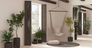 White living room in Boho style, rattan potted plants and lace hanging chair. Window with dark wooden shutters and parquet. 