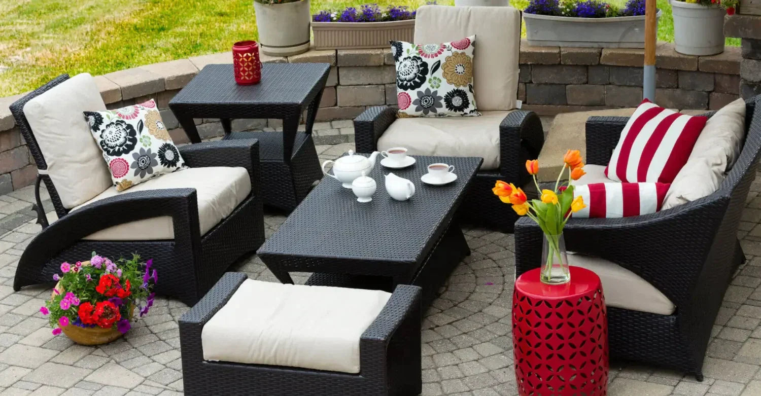 Outdoor furniture set featuring dark wicker chairs and tables on stone paver surface.