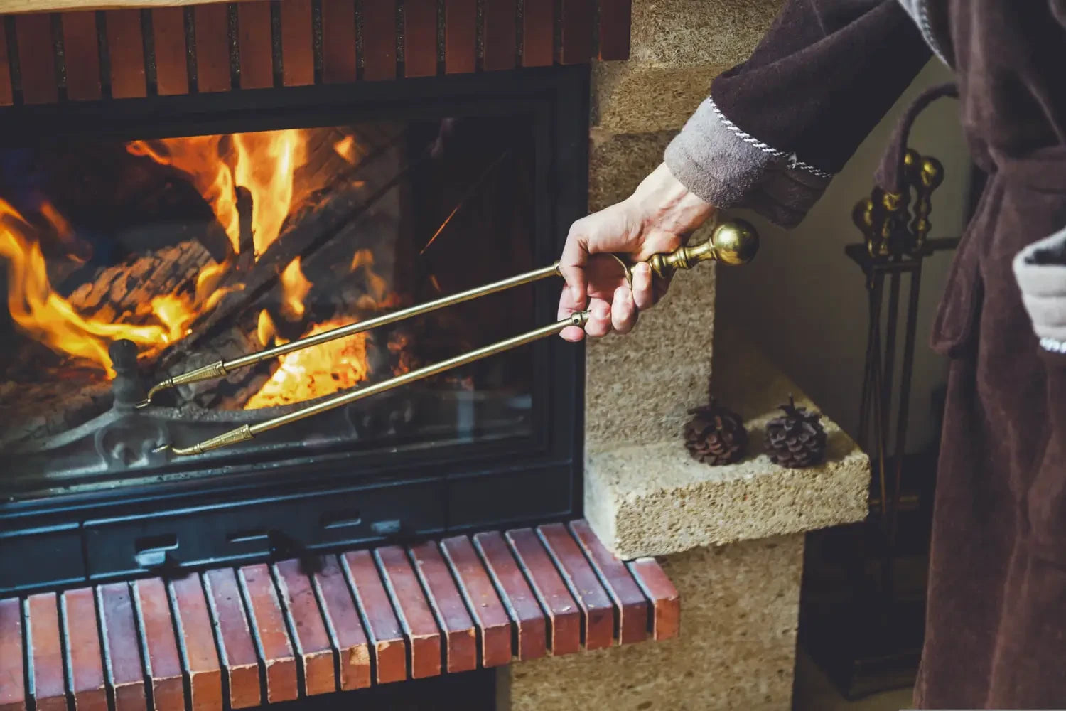 Fireplace tool set being used to tend a roaring fire in a cozy home setting.