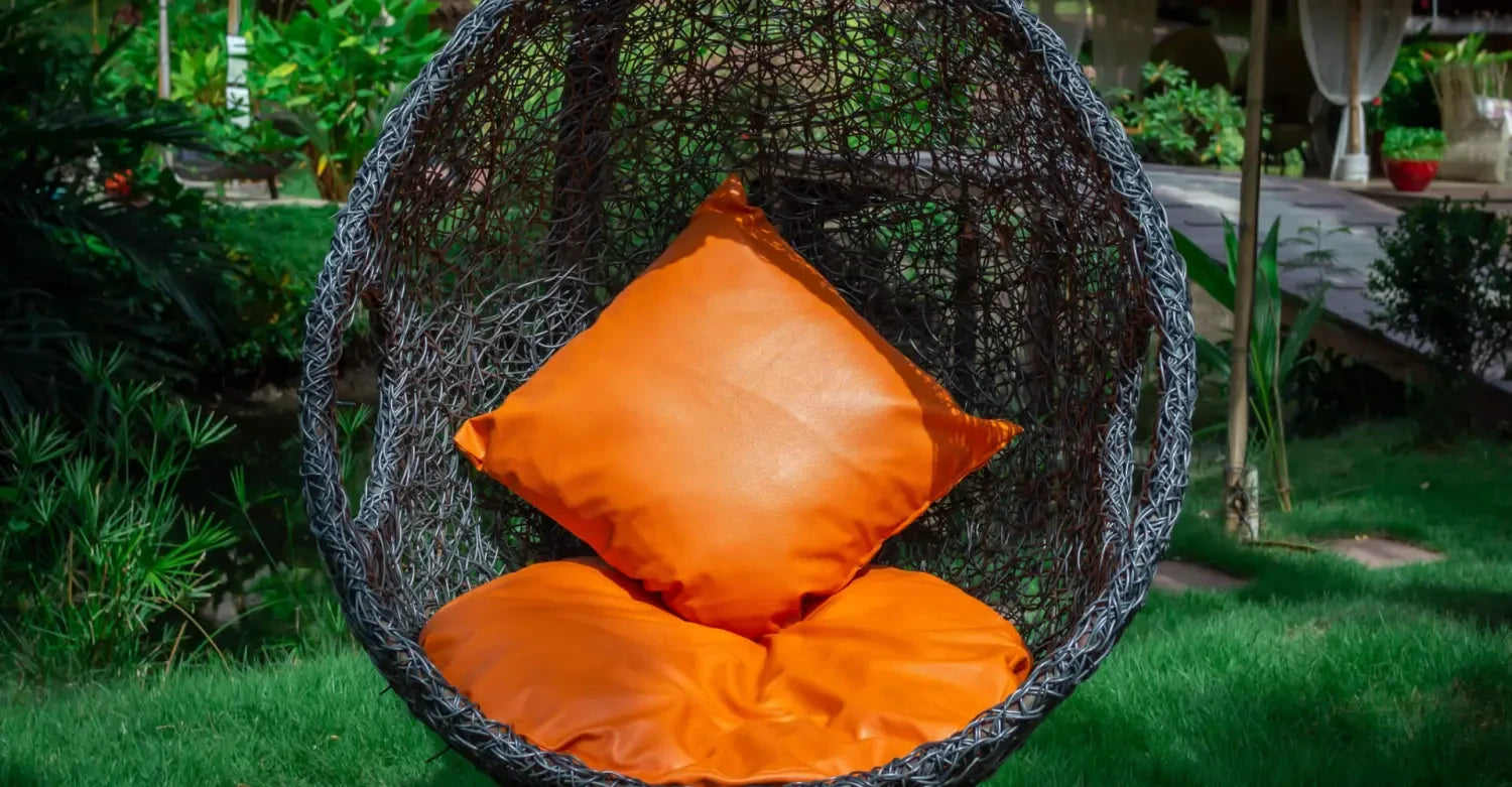 Spherical hanging egg chair with bright orange cushions in a vibrant garden setting.