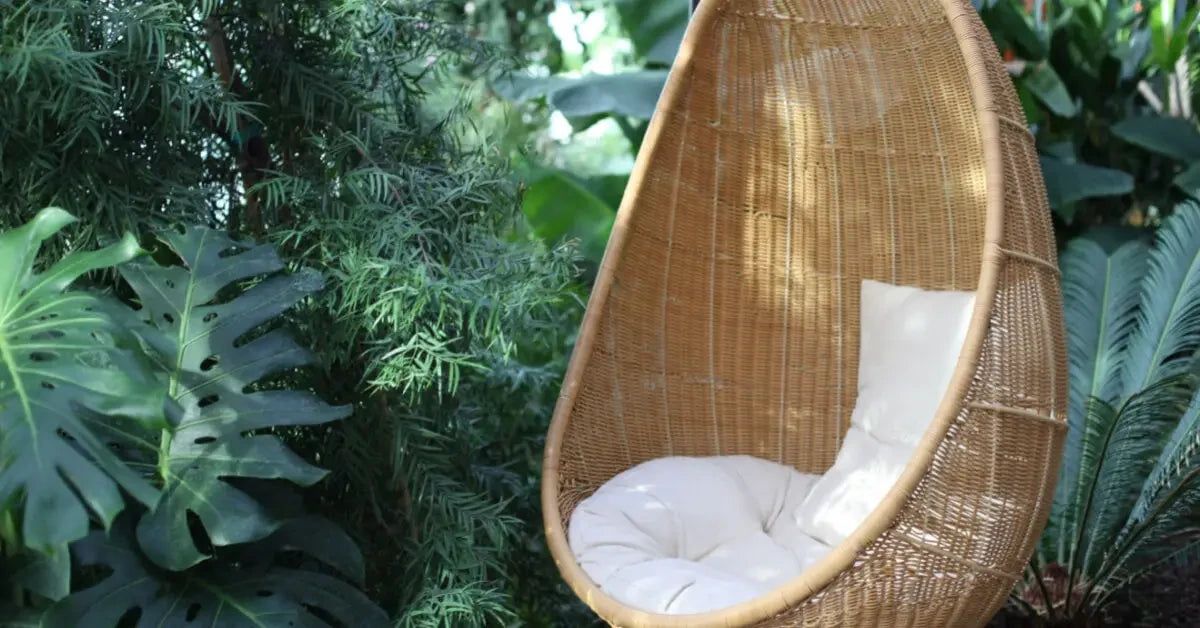 Woven rattan hanging egg chair with white cushion for stylish outdoor seating.