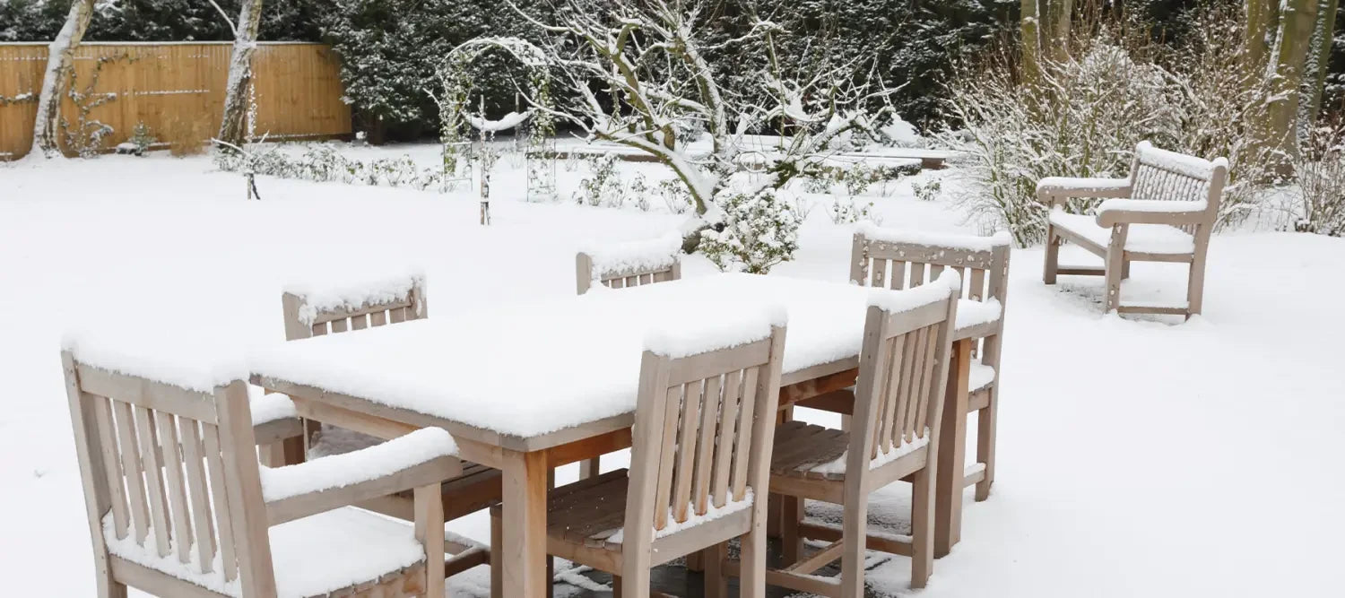 Snow-covered wooden outdoor dining table and chairs with outdoor furniture covers.