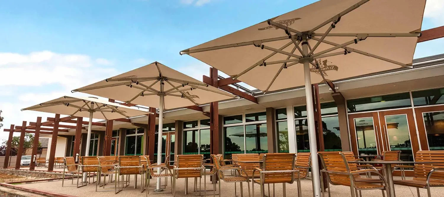 Outdoor patio with wooden furniture under large beige shade umbrellas for instant shade.