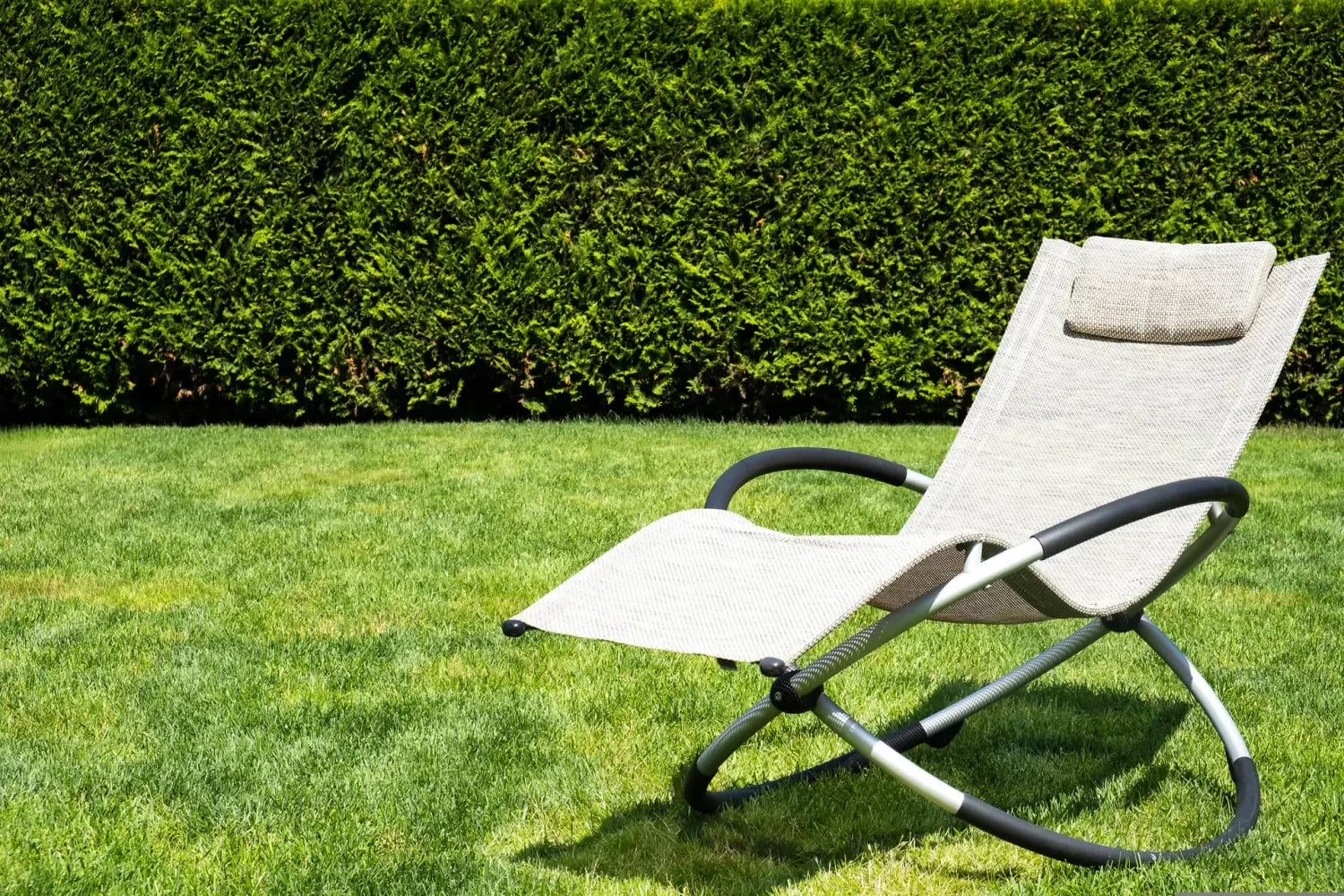White outdoor lounge chair with curved metal frame on grass in sunny garden setting