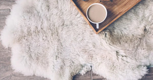 Mug with coffee and home decor on wooden serving tray on sheep skin rug. Winter weekend concept, top view
