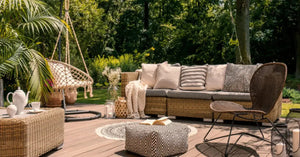 A rattan patio set including a sofa, a table and a chair on a wooden deck in the sunny garden.