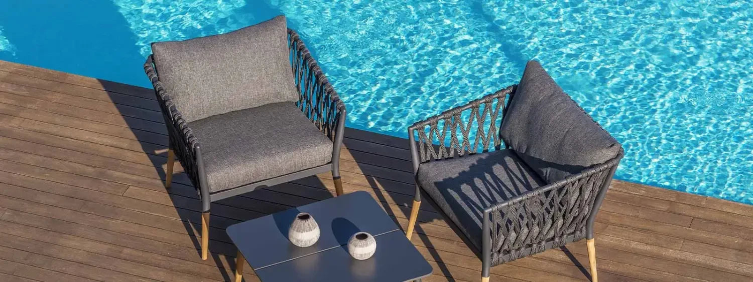 Outdoor lounge chairs set with two chairs and a table by a pool in an outdoor space.