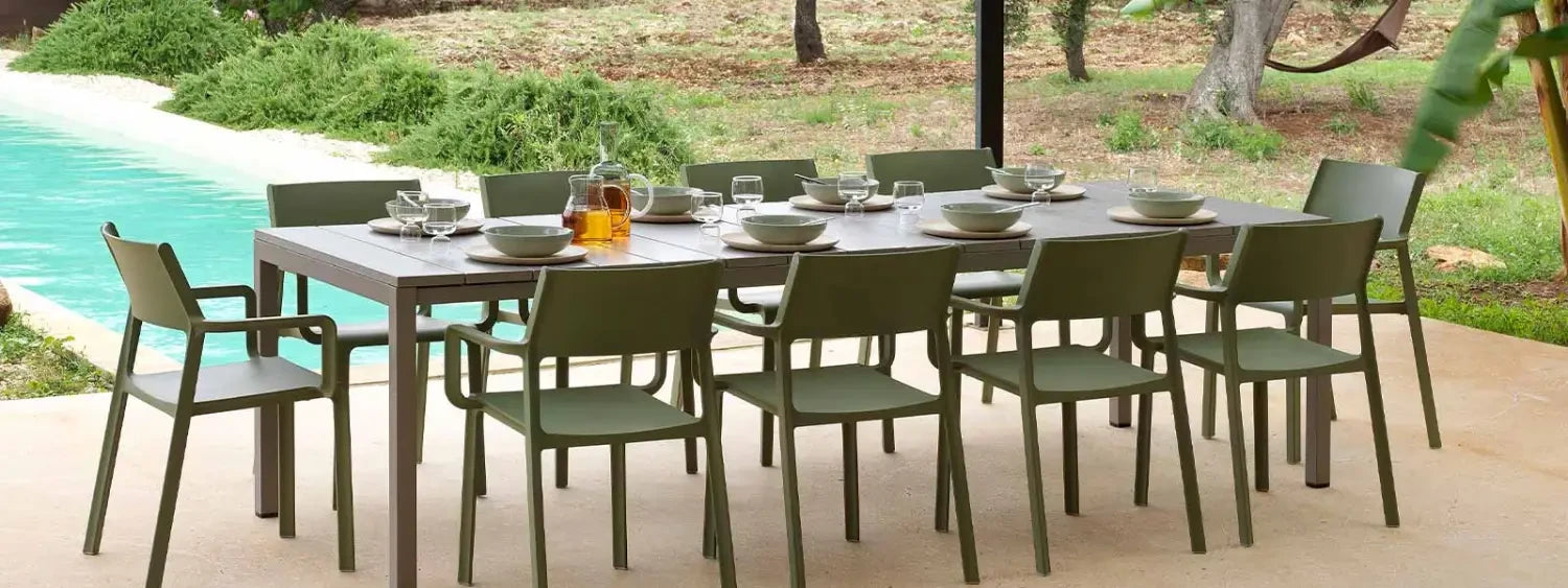 Outdoor dining table set with chairs, plates, and glasses by a pool for stylish gatherings.