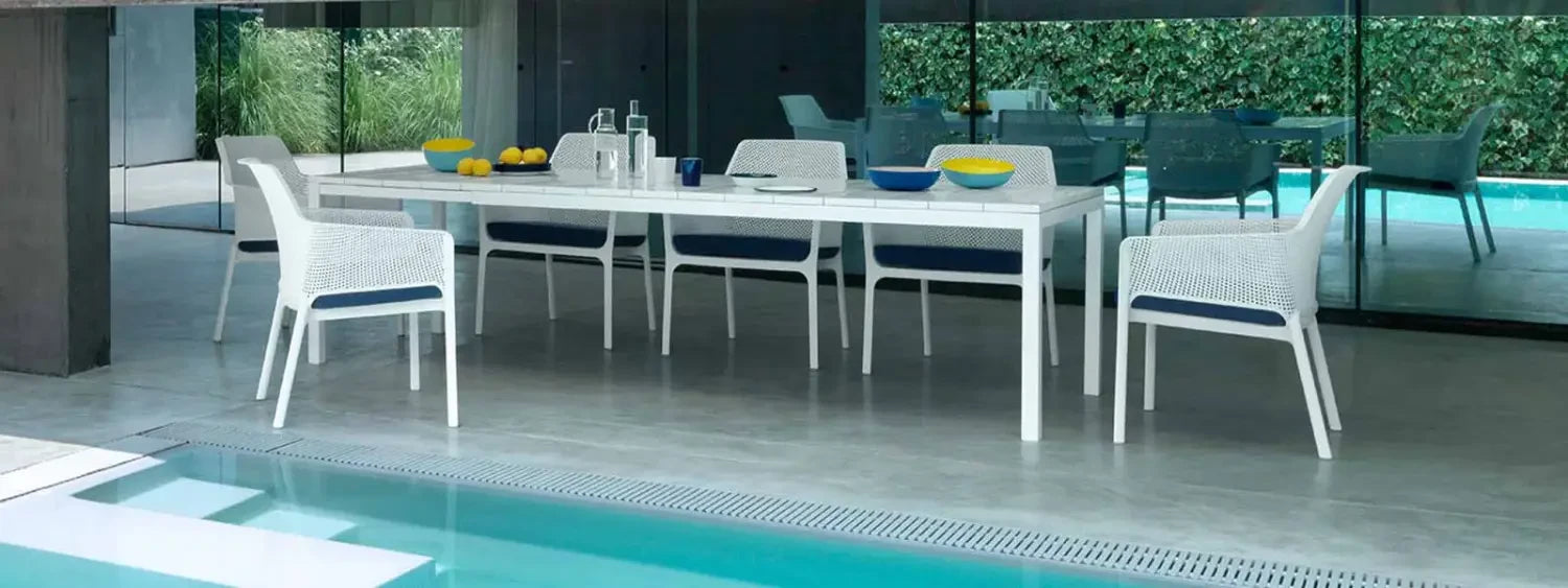 White outdoor dining table with matching chairs beside a pool in an elegant setting.